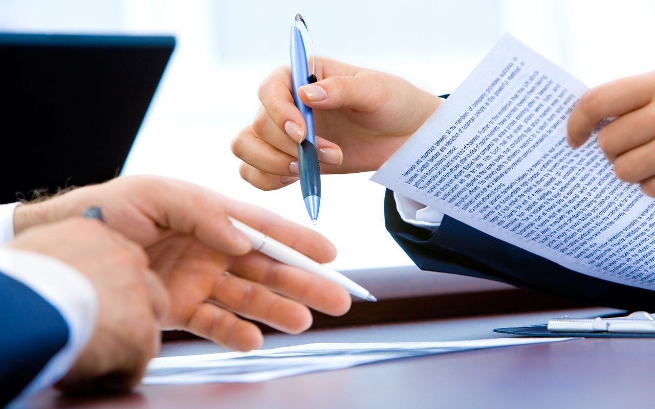 Deux personnes échangeant des documents et des stylos pour la signature d’un contrat de mutuelle d’entreprise