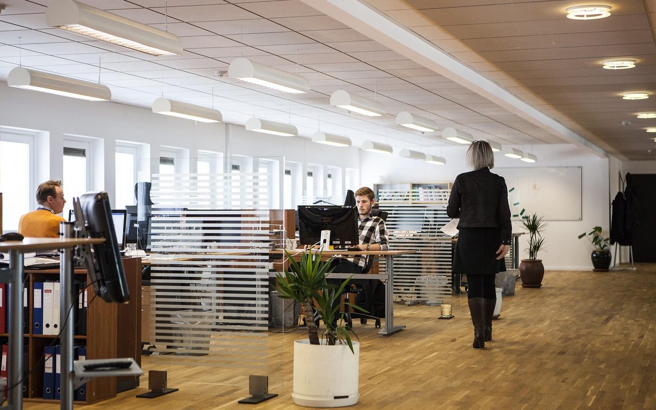 Open space de bureau moderne avec employés travaillant sur ordinateurs et collègue marchant dans l'allée