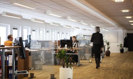 Open space de bureau moderne avec employés travaillant sur ordinateurs et collègue marchant dans l'allée